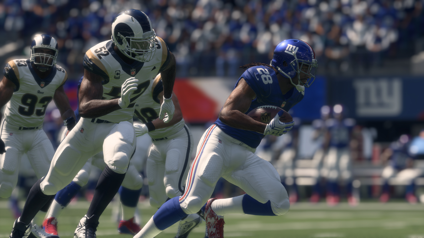 Madden NFL 18 Football player running with the ball in hand while being chased by opponents while crowd watches on in the background